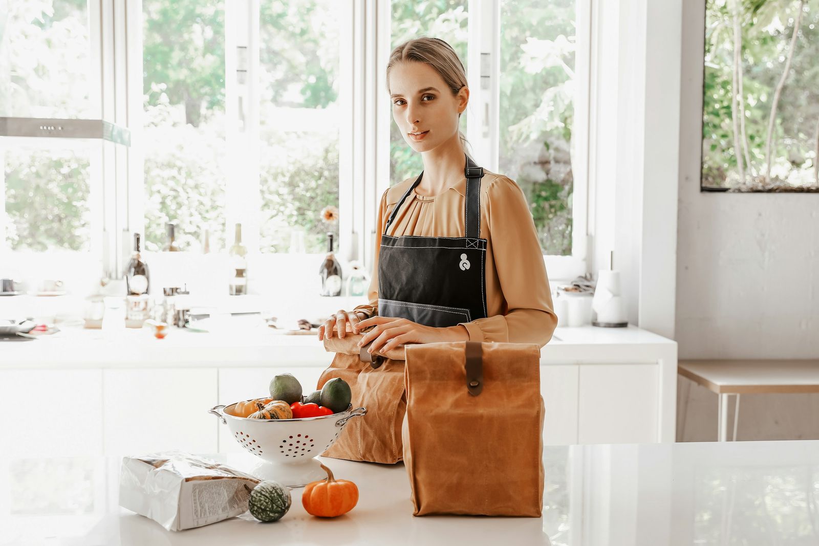 Dans une cuisine lumineuse, une femme en tablier sort des légumes d'un sac de courses posé sur le plan de travail.