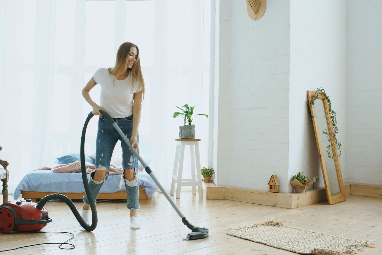 Une jeune femme passe l'aspirateur dans une pièce claire et peu meublée.