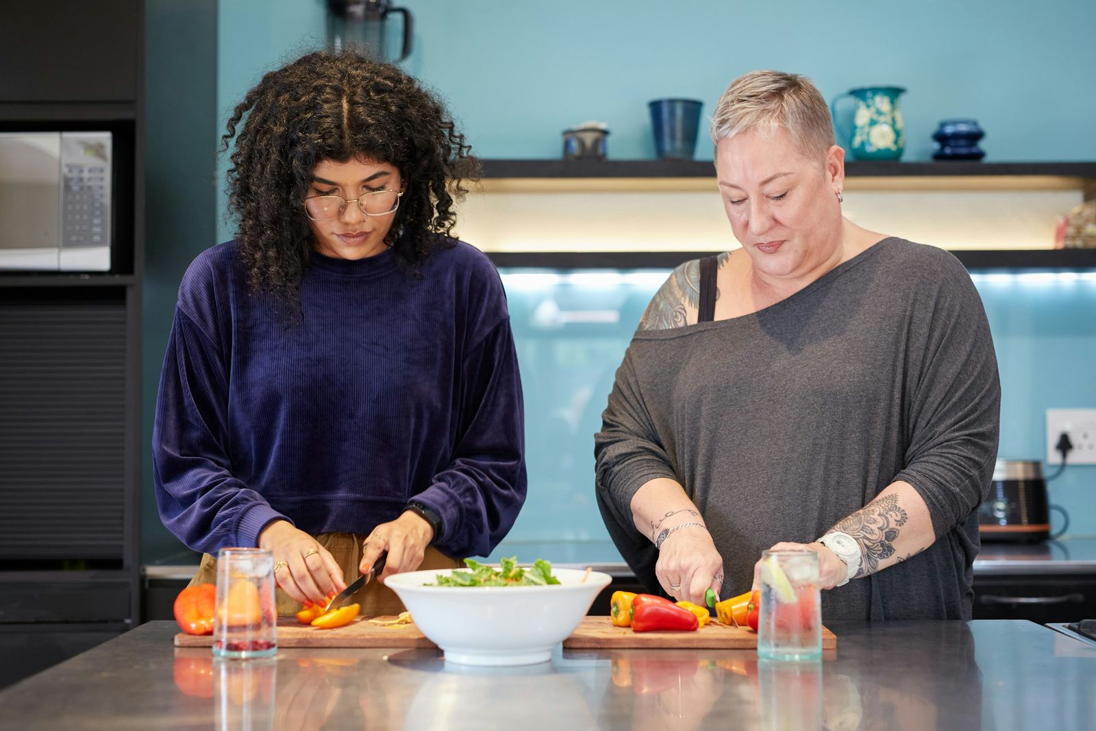 Deux femmes de générations différentes coupent des légumes côte à côte dans une cuisine.