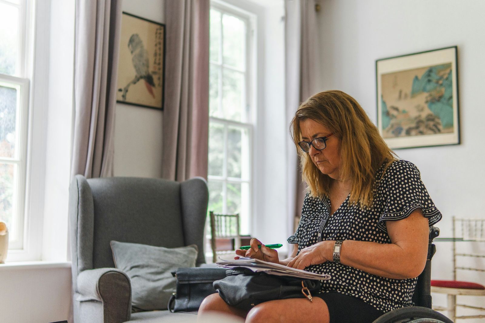 Une femme en fauteuil roulant prend des notes sur des documents dans son salon.