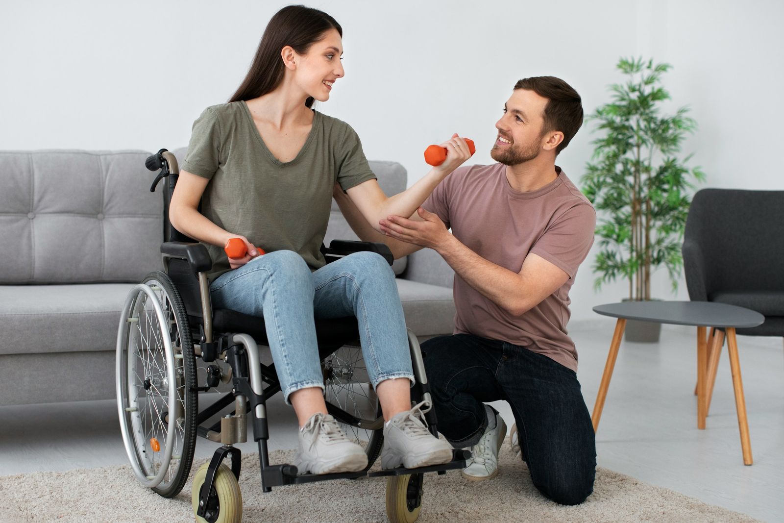 Dans un salon, un professionnel accompagne une jeune femme en fauteuil roulant qui soulève de petits haltères.